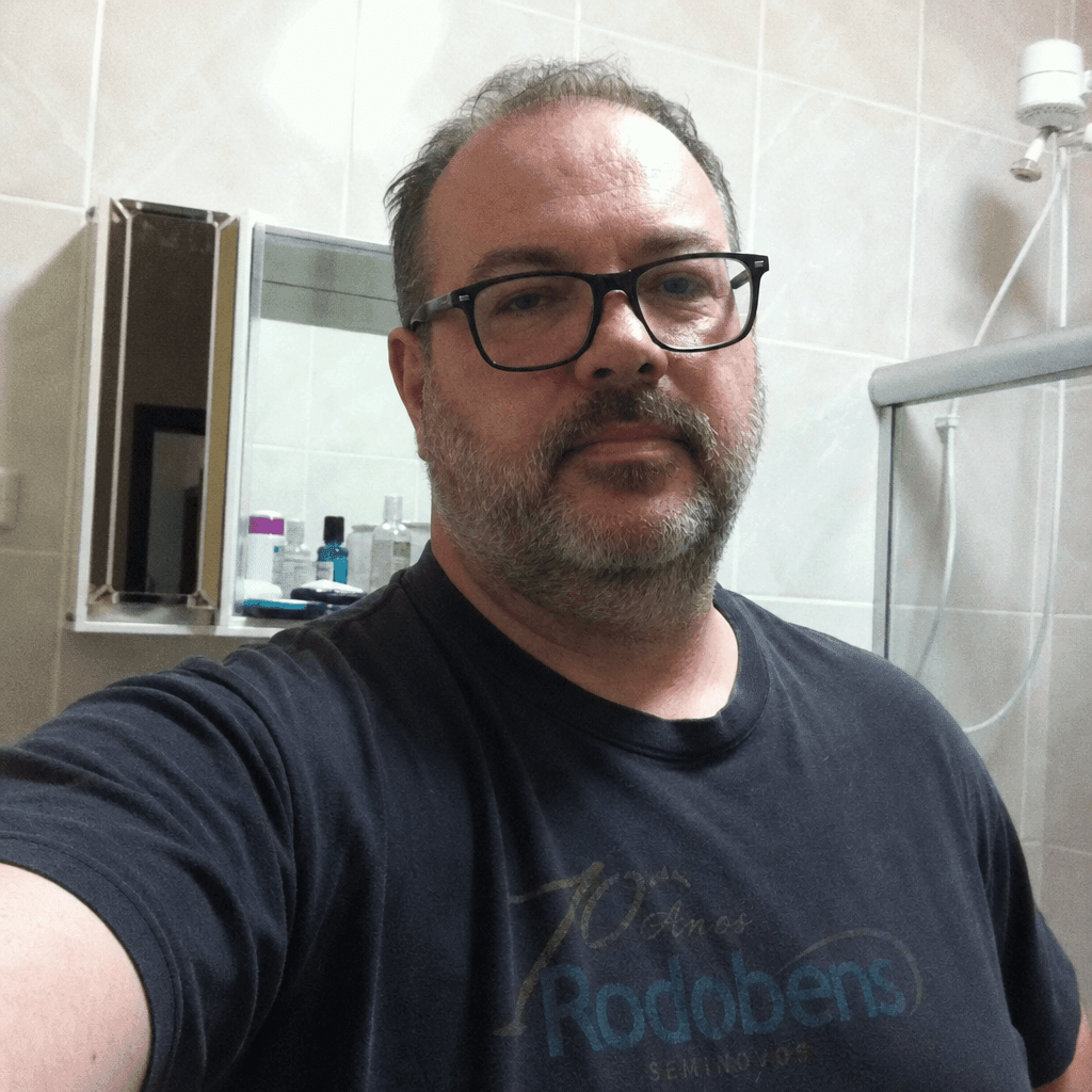 Homem branco maduro em camiseta polo casual, selfie em ambiente residencial com luz amarelada — exemplo de foto informal
