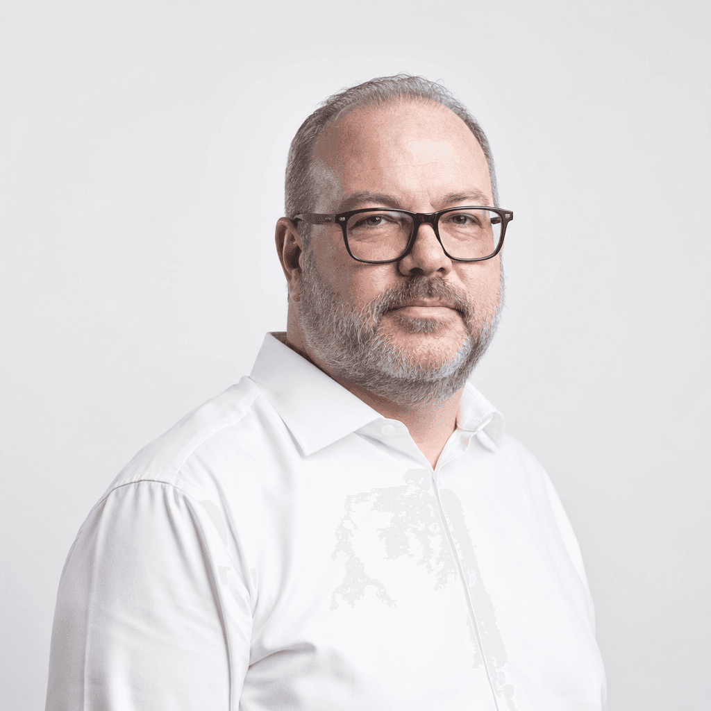 Mesmo homem em camisa branca social, óculos, barba aparada, fundo cinza claro neutro, expressão séria mas acessível — foto profissional